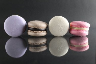 Dört kek, mavi pembe kahve, beyaz makaronlar aynalı bir yüzeye uzanıyorlar ve siyah bir arkaplan üzerine yansıtılıyorlar..