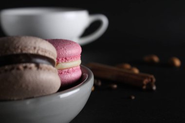 Arkadaki tabakta bir fincan kahve ya da çay, kahve çekirdeği ve siyah arka planda tarçın bulunur. .