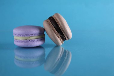 İki badem kurabiyesi lavanta ve kahve çikolatası mavi arka planda uzanıyor. Yansımalı ve metin için bir yer ve kopyalanacak bir yer var..