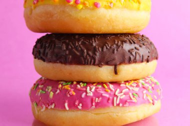 Pembe arka plan üzerine serpiştirilmiş üç tane Berlinli donut pembe çikolatası..