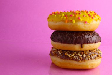 Tatlı natürmort berliner arkada, parlak pembe arka planda üç çörek sarısı bir yığın uzanıyor.