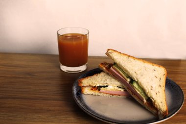 Sosisli, salatalıklı, yeşil salatalıklı sandviçli kahvaltı sandviçi bir bardak portakal şeftali suyunun yanında duruyor. Avrupa kahvaltısı.