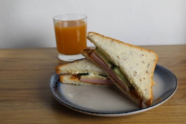 Sosisli, salatalıklı, yeşil salatalıklı sandviçli kahvaltı sandviçi bir bardak portakal şeftali suyunun yanında duruyor. Avrupa kahvaltısı.