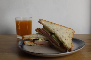 Sosisli, salatalıklı, yeşil salatalıklı sandviçli kahvaltı sandviçi bir bardak portakal şeftali suyunun yanında duruyor. Avrupa kahvaltısı.