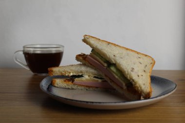 Sosisli, salatalıklı öğle yemeği sandviçi bir fincan çay ya da kahvenin yanında duruyor. Sabah servisi. Hazırlık. Cafe Restoranı.