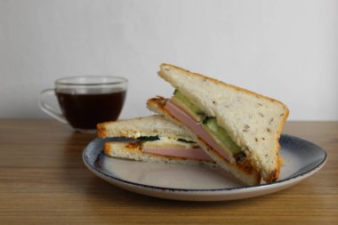 Sosisli, salatalıklı öğle yemeği sandviçi bir fincan çay ya da kahvenin yanında duruyor. Sabah servisi. Hazırlık. Cafe Restoranı.