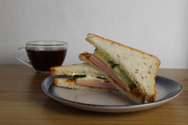 Sosisli, salatalıklı öğle yemeği sandviçi bir fincan çay ya da kahvenin yanında duruyor. Sabah servisi. Hazırlık. Cafe Restoranı.