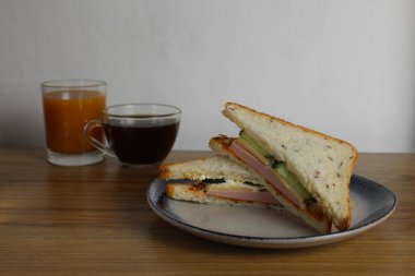 Sosisli, salatalıklı öğle yemeği sandviçi bir fincan çay ya da kahvenin yanında duruyor. Sabah servisi. Hazırlık. Cafe Restoranı.