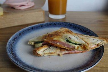 Jambonlu ve sebzeli sandviç meyve suyunun yanındaki tabağa konur. Kahvaltı hazırlıyorum. Atıştırmalık.