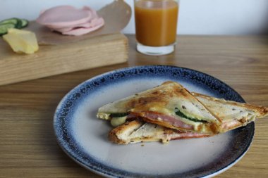 Jambonlu ve sebzeli sandviç meyve suyunun yanındaki tabağa konur. Kahvaltı hazırlıyorum. Atıştırmalık.