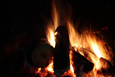 Karanlıkta siyaha yakın dumanlı şenlik ateşi. Yanan odun, odun.