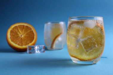 Adım adım limonata pişirme talimatı. Üçüncü adım. Su, portakal ve buzlu içecek hazır. Mavi arka planda portakallı limonata. Yaz içeceği.