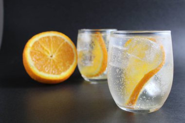 Portakallı limonata ve buzlu buzlu siyah arka planda buz ve portakalın yanında. Siyah arka planda yaz içkisi.