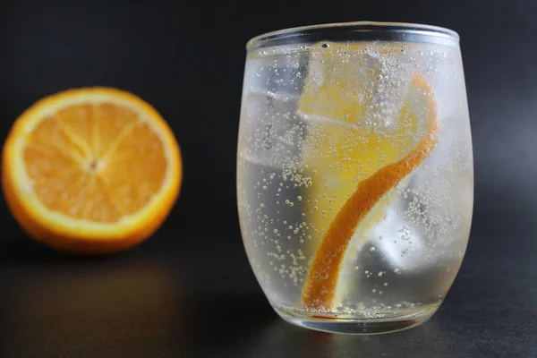 lemonade with orange and ice in a glass on a black background next to lies ice and orange. Summer drink on a black background.