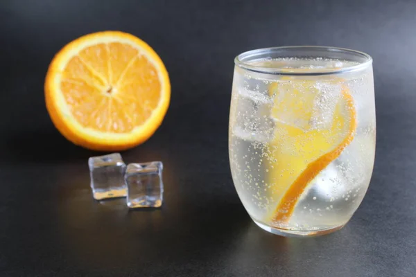 lemonade with orange and ice in a glass on a black background next to lies ice and orange. Summer drink on a black background.