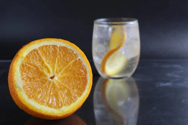 lemonade with orange and ice in a glass on a black background next to lies ice and orange. Summer drink on a black background.