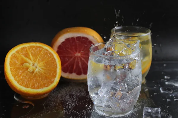 Bir bardak su ve buzun üzerine su sıçradı. Meyve, portakal, greyfurt ve buz yakınlarındadır. Siyah bir arka planda. Soğuk içecek ferahlatıcı..