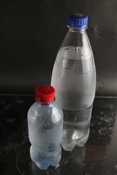 Cold water in a bottle on a black background. A bottle of water stands on a black background. Cool summer drinks.