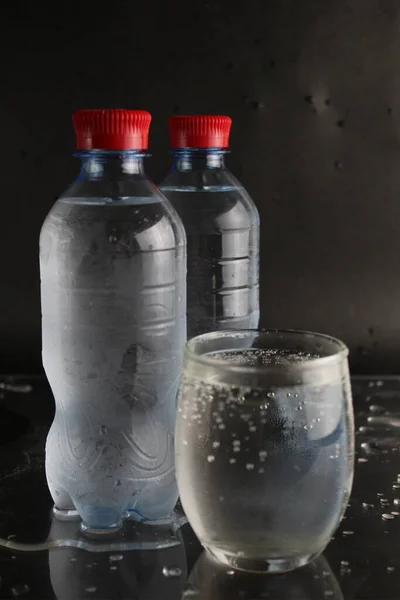 玻璃杯和塑料瓶中的矿泉水站在黑色背景旁边 旁边有一个插入的地方和一个铜版块 — 图库照片