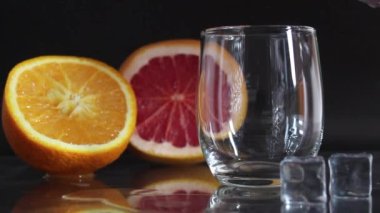 Meyve portakalı greyfurt ve buzun yanındaki siyah arkaplanda bardağa su döker.