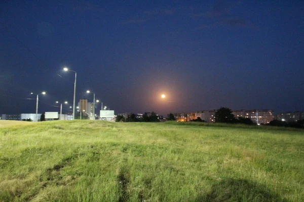 ランタンの光の下で夜の街の郊外にある月 夜景月を草の上に — ストック写真