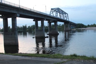 Akşam alacakaranlıkta nehir üzerinde mavi soğuk renklerde bir köprü. Şehir manzarası.