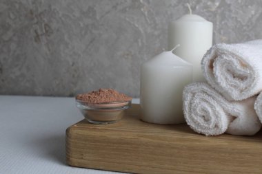 Spa tedavileri dinleniyor. Yağlı kil, mum maskeli beyaz havlu masajı için beyaz gri beton arka plan yakın plan görüşlü ahşap bir tepsiye konur. Evde vücut bakımı.