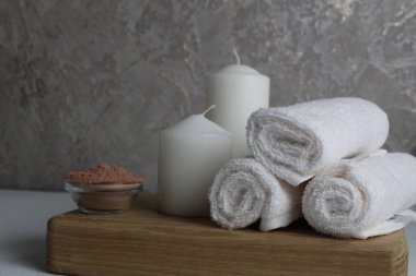 Spa tedavileri gevşetir. Evde vücut bakımı. Beyaz havlu mumları, banyo için tuz, gri bir arka planda, ahşap bir tepside yatar..