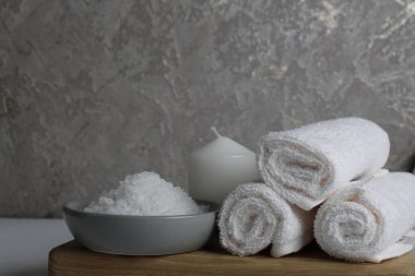 Spa tedavileri gevşetir. Evde vücut bakımı. Beyaz havlu mumları, banyo için tuz, gri bir arka planda, ahşap bir tepside yatar..
