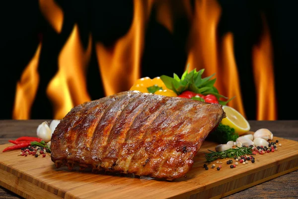 Grilled pork ribs and various vegetables on a chopping wood — Stock Photo, Image