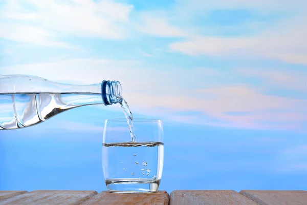 新鲜和清洁的饮用水被从瓶往杯子里倒上天空背景 — 图库照片