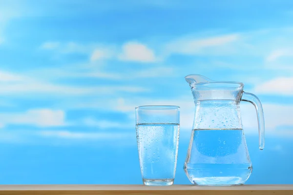 在水罐和玻璃的天空背景上的新鲜和干净的饮用水 — 图库照片