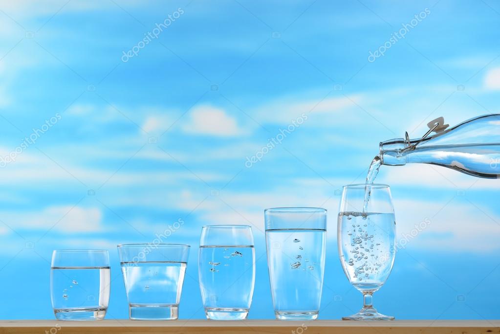 Fresh and clean drinking water being poured from bottle into glass on sky background Stock Photo