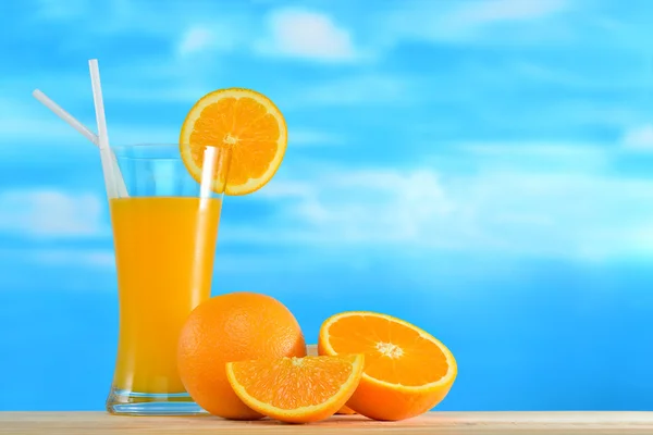 Sok pomarańczowy i kawałkami pomarańczy na tle nieba — Zdjęcie stockowe