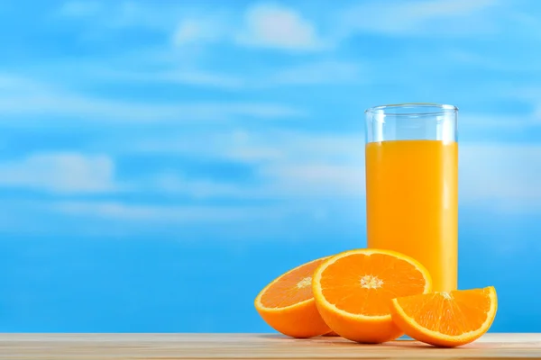 Sok pomarańczowy i kawałkami pomarańczy na tle nieba — Zdjęcie stockowe