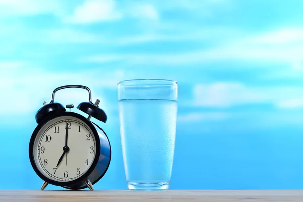 Fresh and clean drinking water in glass and alarm clock on sky background — Stock Photo, Image