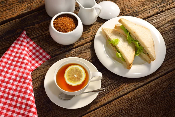 Чашка чая с лимоном и сэндвичем на деревянном фоне — стоковое фото