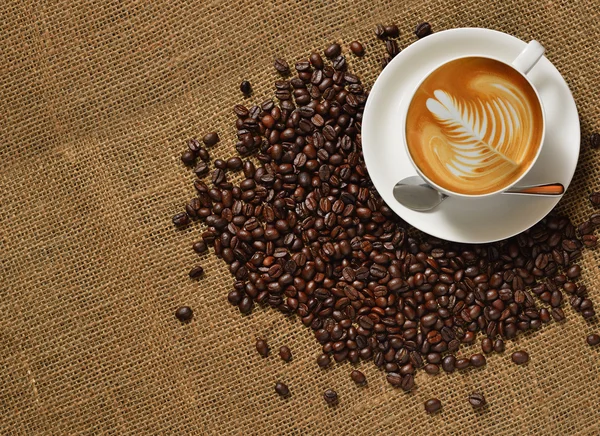 Vista dall'alto, Tazza di caffè latte e chicchi di caffè su sfondo iuta — Foto Stock