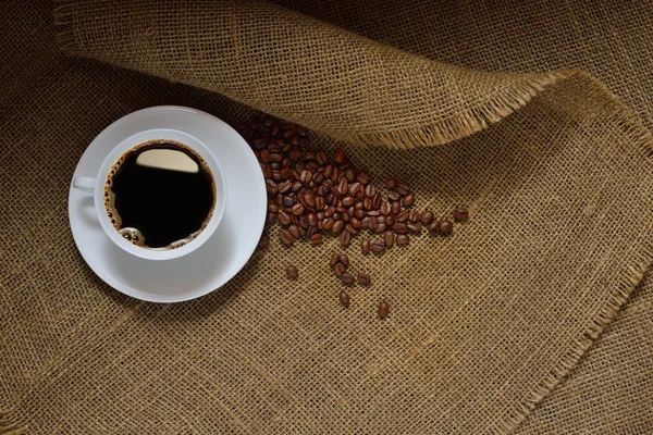Vista dall'alto della tazza di caffè e chicchi di caffè su sfondo iuta — Foto Stock