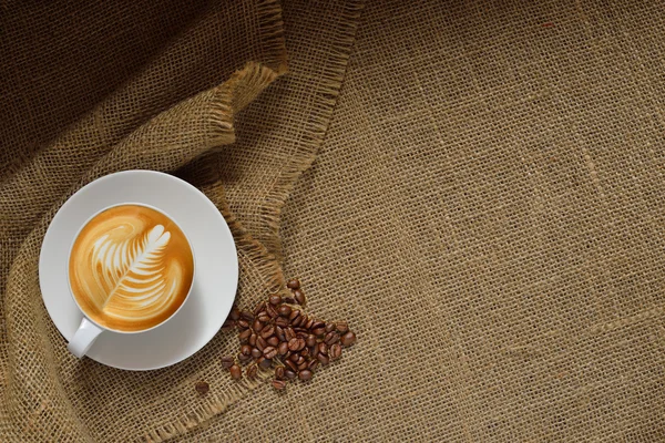 Vista dall'alto di tazza di caffè latte e chicchi di caffè su sfondo iuta — Foto Stock