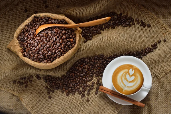 Vista superior da xícara de café latte e grãos de café no fundo da serapilheira — Fotografia de Stock