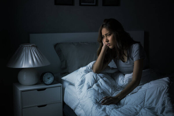 Depressed young Asian woman sitting in bed cannot sleep from insomni