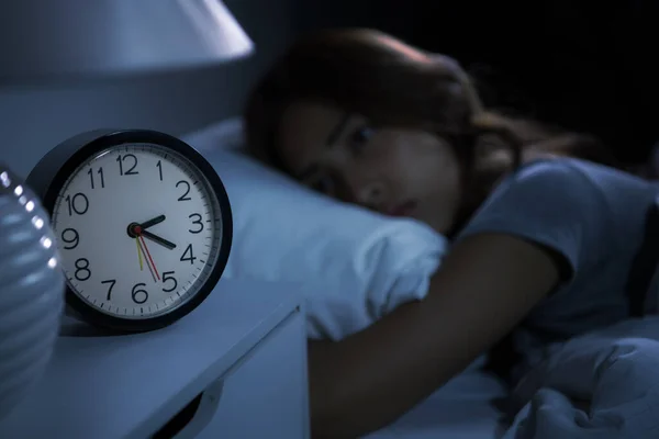 寝たきりの若い女は不眠症で寝られない 目覚まし時計の選択的フォーカス — ストック写真