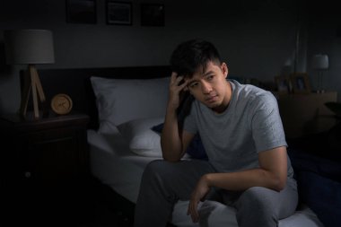 A depressed young man suffering from insomnia sitting in bed clipart