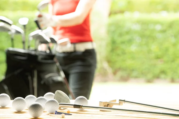 Golf balls, golf equipment, and golf club on the table on driving range with the golfer in background
