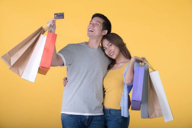 Sarı arka planda kredi kartı ve alışveriş torbaları tutan Asyalı çift.