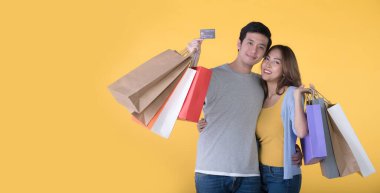 Sarı arka planda kredi kartı ve alışveriş torbaları tutan Asyalı çift.