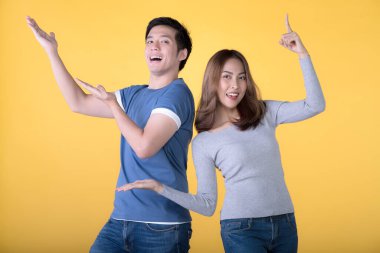 Mutlu Asyalı çift parmaklarını kaldırıp sarı arka plandaki kameraya bakıyor.