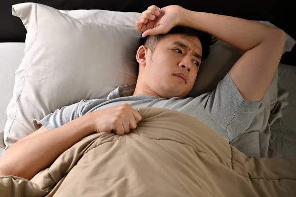 Depressed young Asian man lying in bed cannot sleep from insomnia