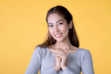 Sarı arka planda dikilip kameraya bakan sıradan giyinmiş güzel, gülümseyen Asyalı bir kadının portresi.